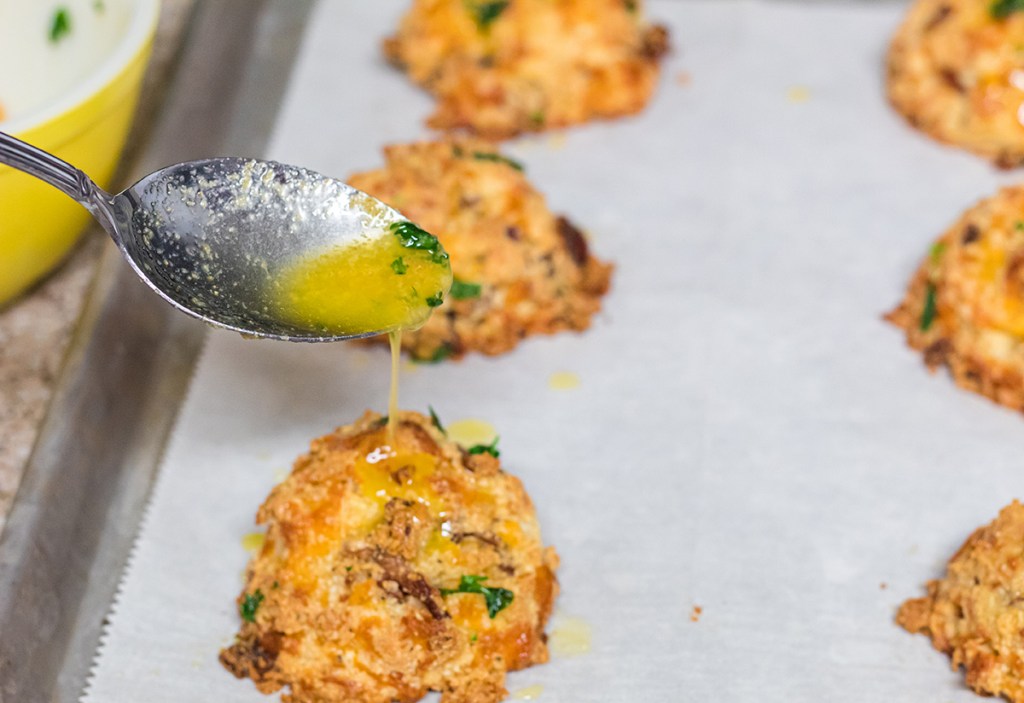 pouring butter on keto loaded cheddar bacon biscuits