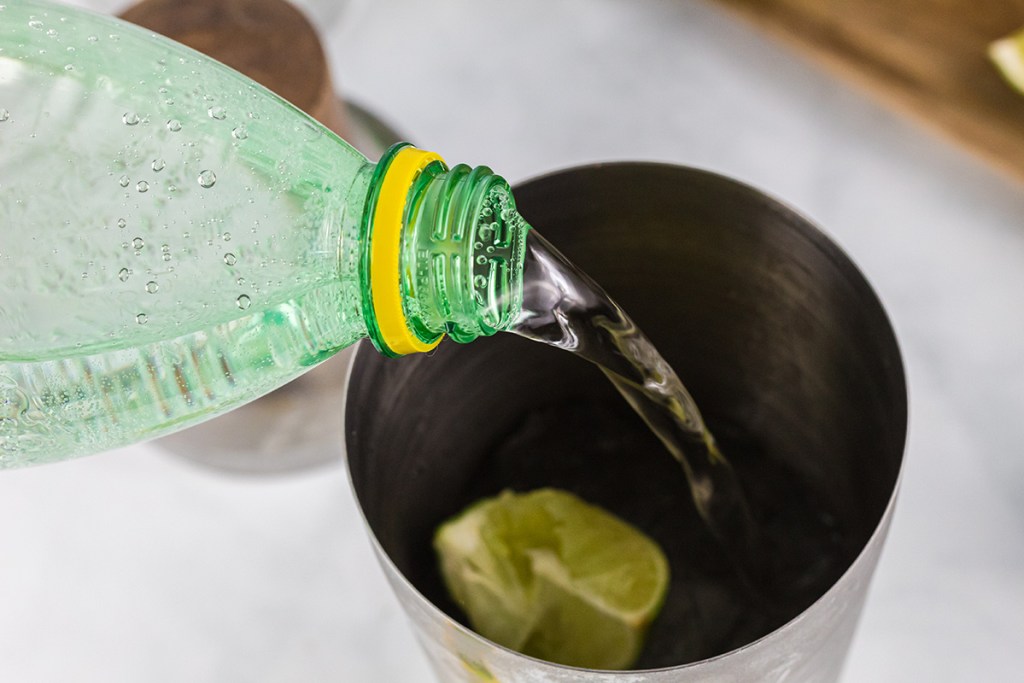 pouring sparkling water into cocktail shaker for margarita