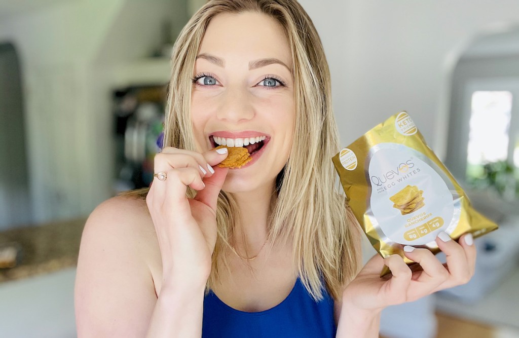 woman biting chips while holding gold and white bag