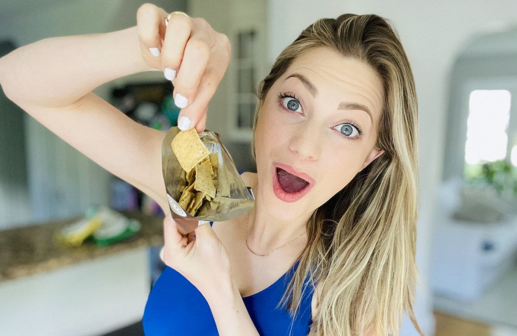 woman holding up bag of open chips with surprised face