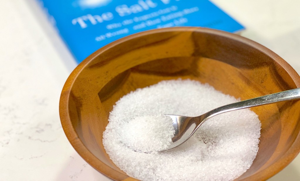 wood bowl full of salt with spoon inside and the salt fix book in background