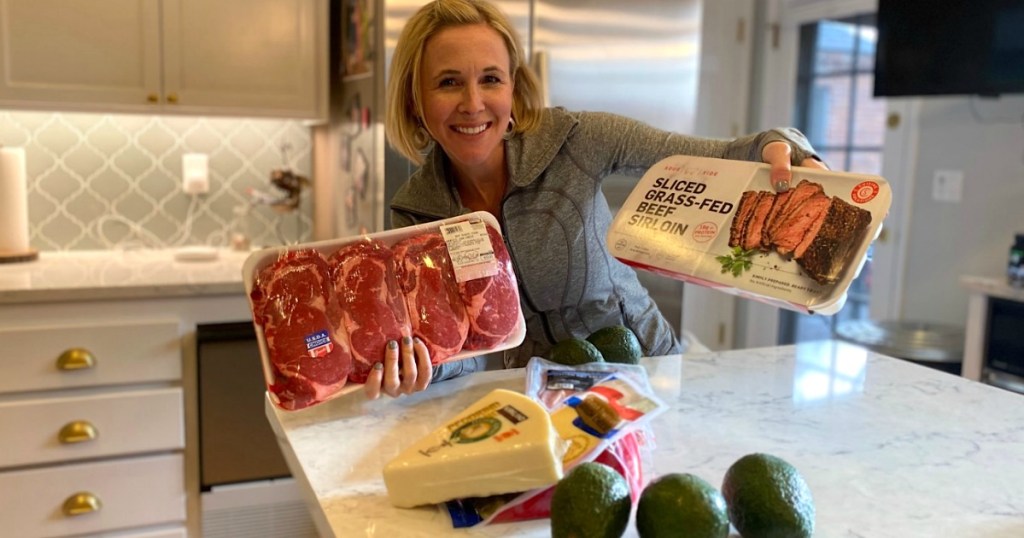 woman in kitchen holding two large meat packages from Costco