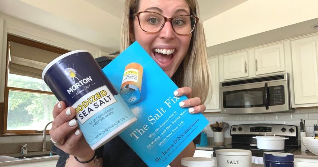 A woman holding a book and some salt in a kitchen