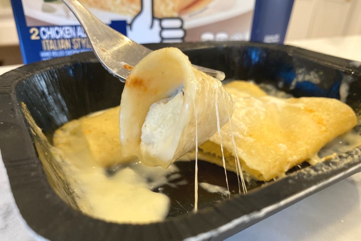 A fork cutting into Real good Foods chicken alfredo enchiladas in entree dish