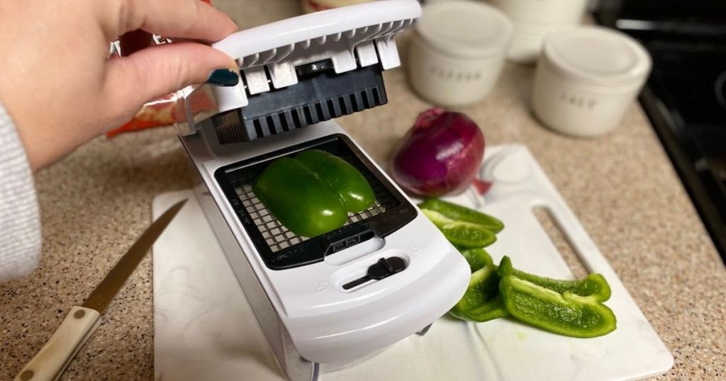 A hand using a veggie chopper on a green pepper