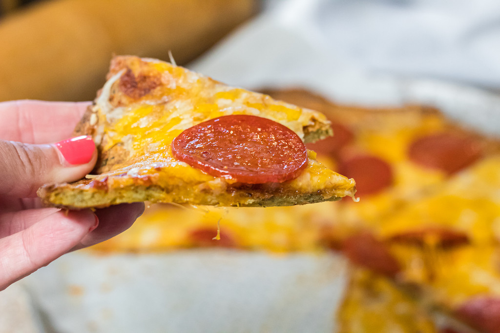 holding keto pork rind pizza slice with pepperoni and cheese 