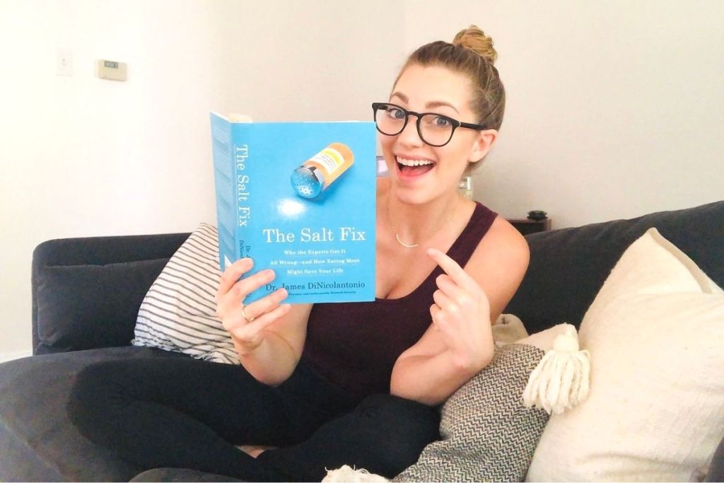 A woman sitting on a couch holding a book and pointing to it