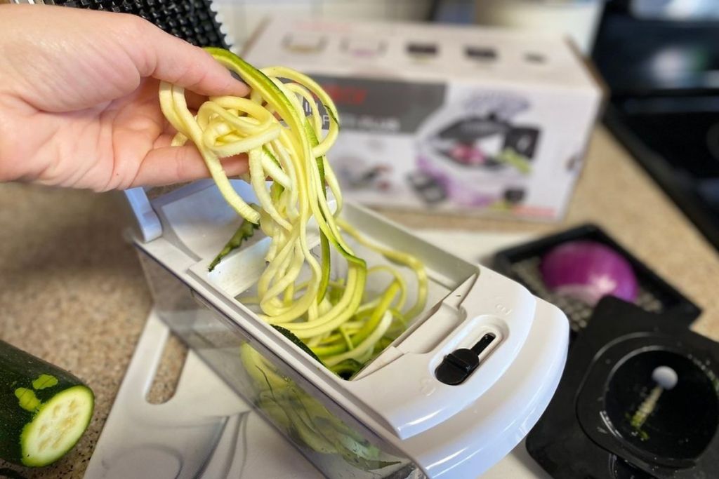 A hand grabbing zucchini noodles out of a veggie chopper