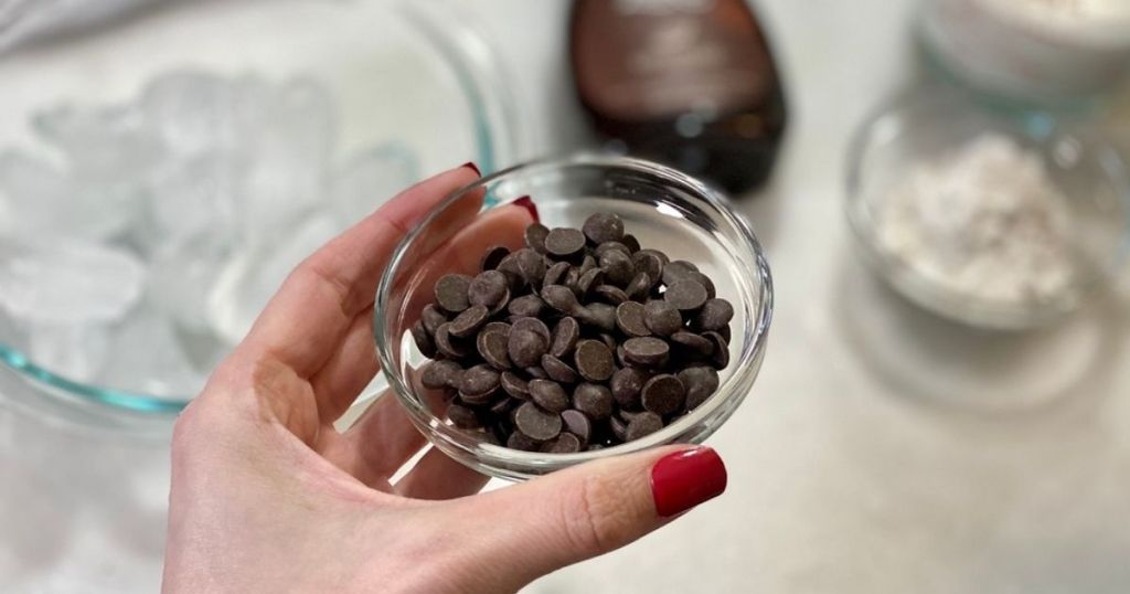 A hand holding a small bowl of chocolate chips