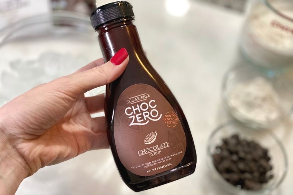A hand holding a bottle of ChocZero chocolate syrup
