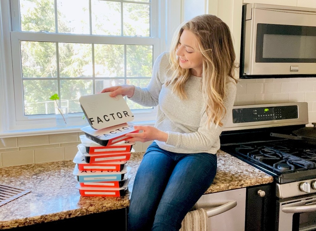 woman sitting on counter looking at stack of factor meals