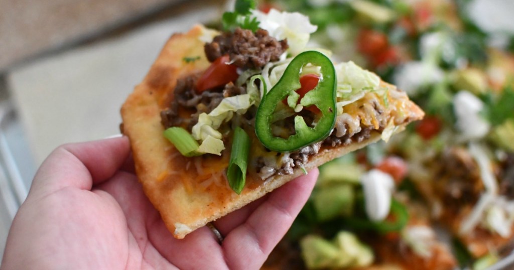 holding slice of keto taco pizza with jalapeno