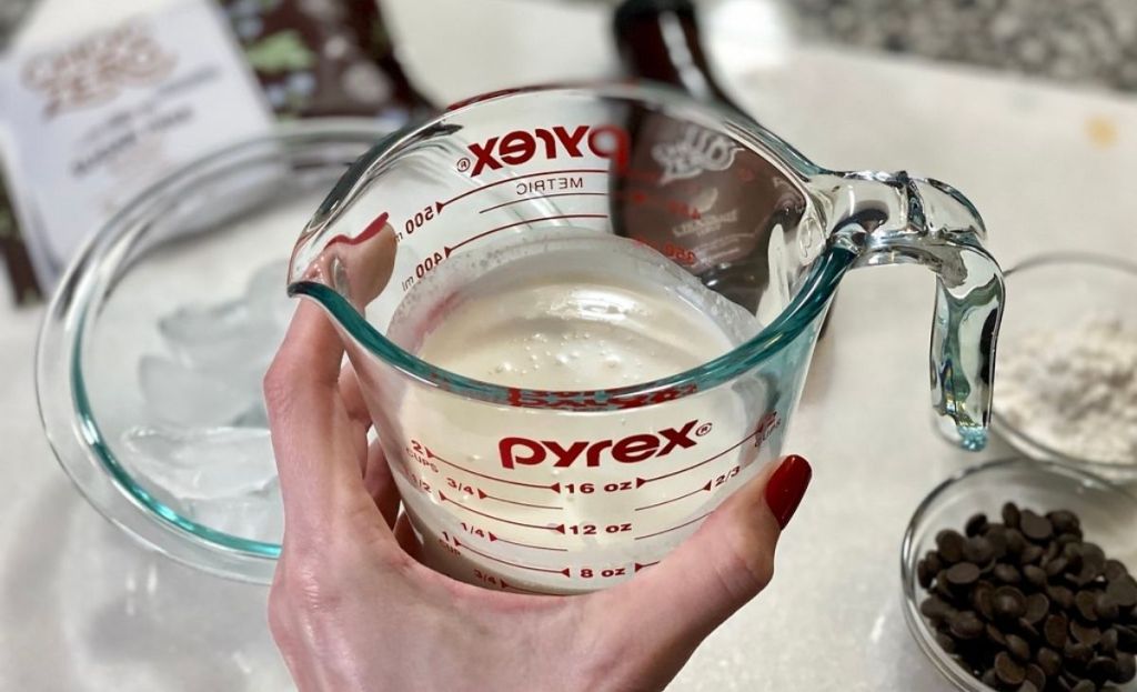 A hand holding a measuring cup with milk in it