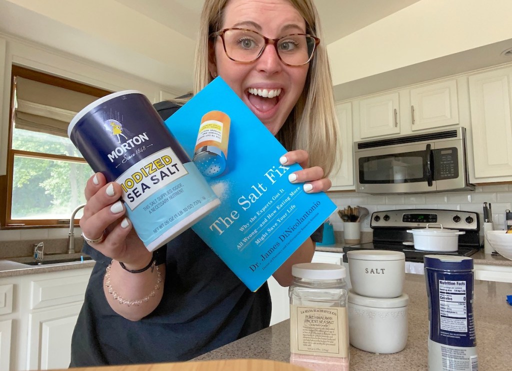 woman smiling holding the salt fix book with iodized jar of salt