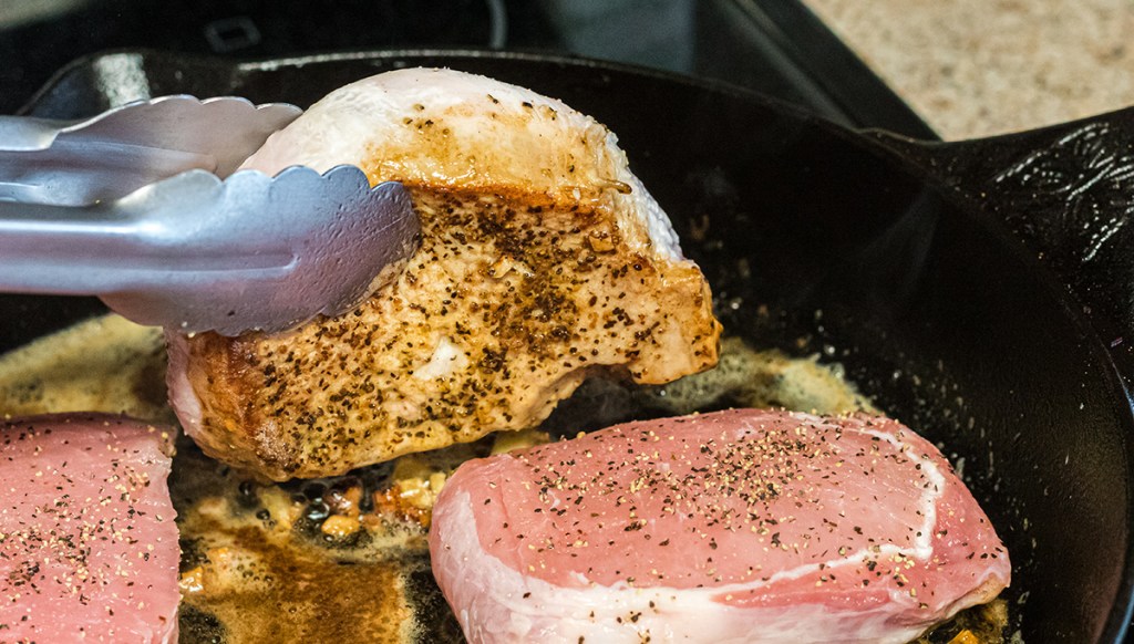 tongs holding seared pork chop in cast iron skillet