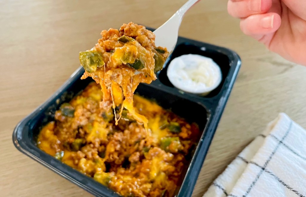 hand holding fork with food from frozen dinner tray