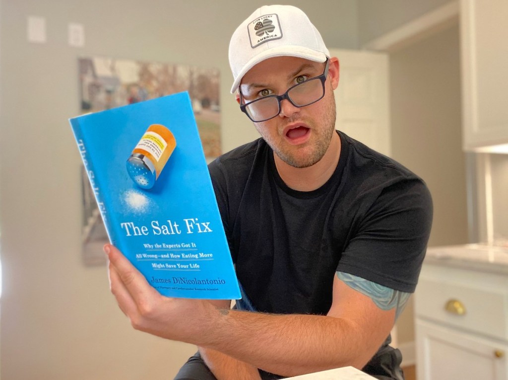 man holding the salt fix book wearing black glasses and white hat