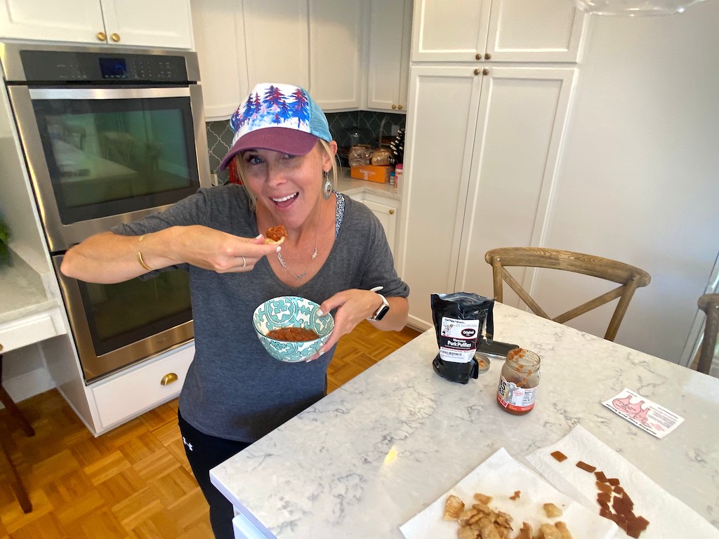 woman eating pork rinds with salsa in kitchen