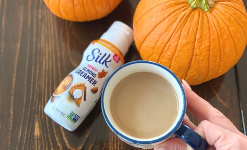 A hand holding a cup of coffee next to some creamer and pumpkins on a table