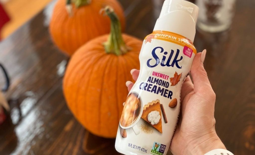 A hand holding some pumpkin creamer in front of pumpkins 