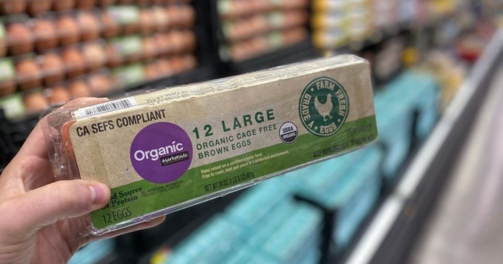 A hand holding up a carton of eggs at a store