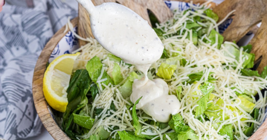 drizzling caesar dressing over salad