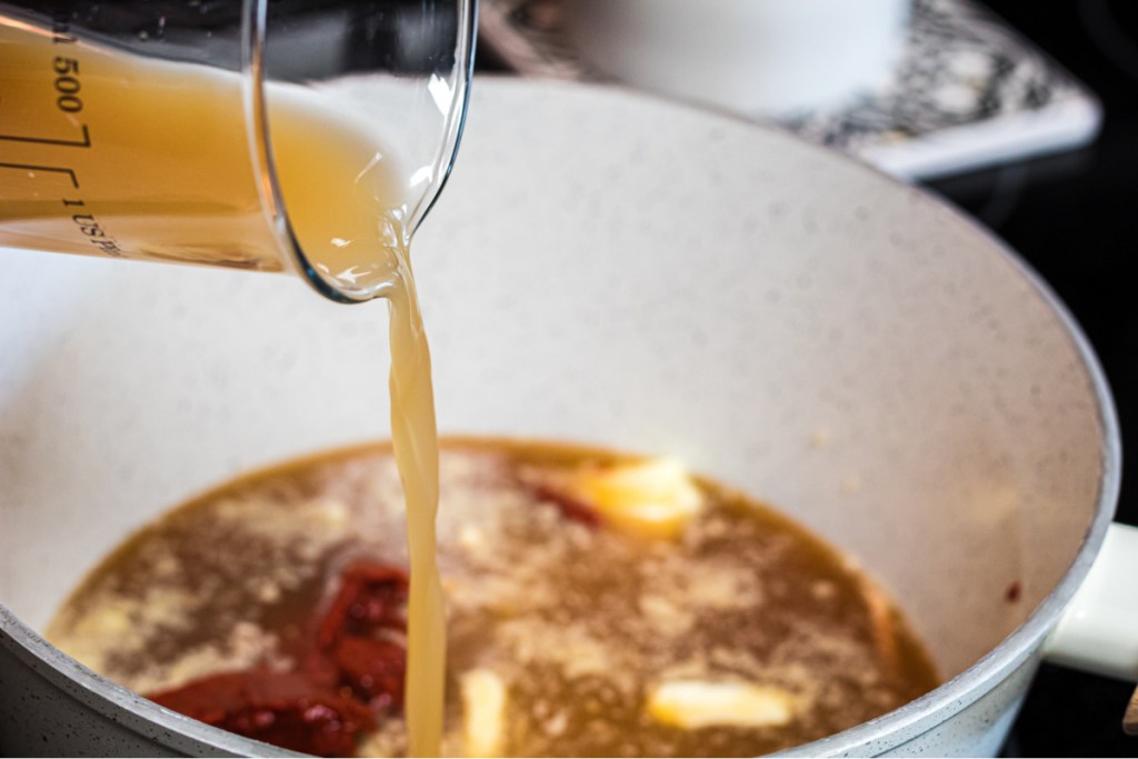 pouring chicken broth into saucepan