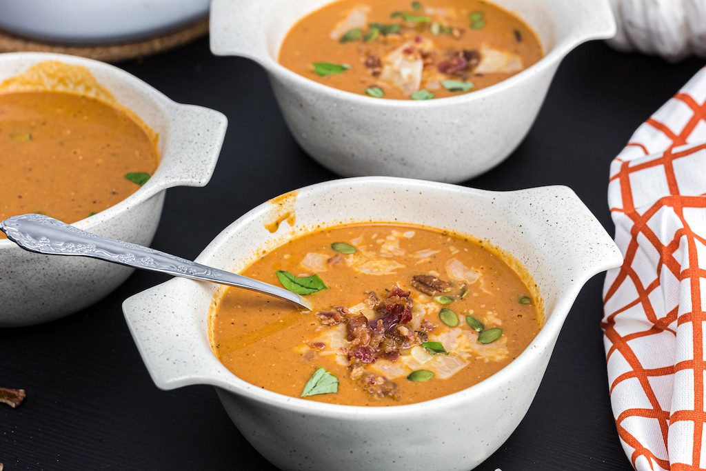 soup bowls filled with keto pumpkin soup and pumpkin seeds & bacon on top