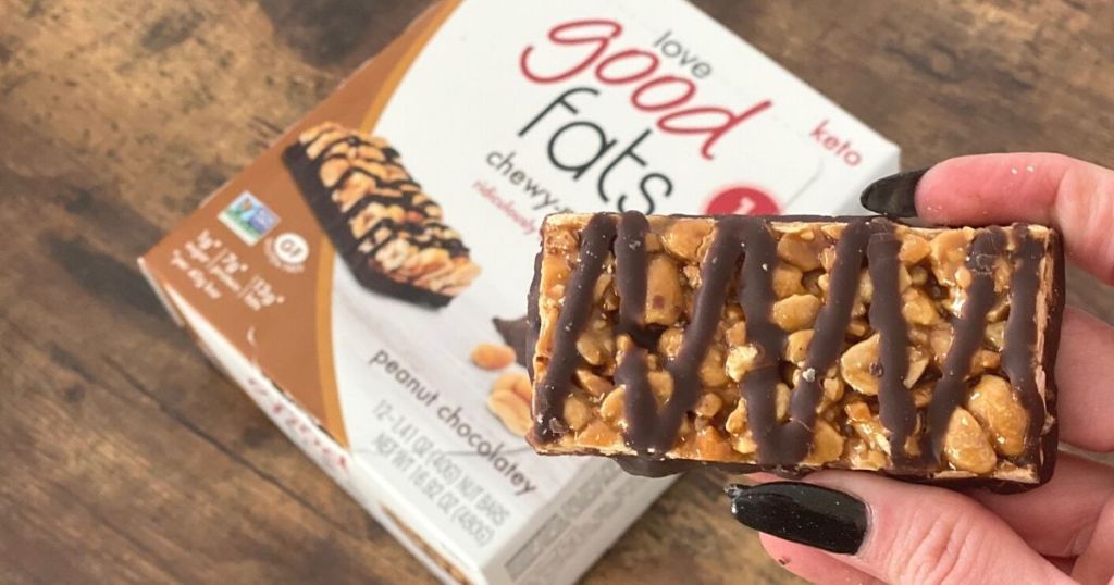 A hand holding a nut bar next to the box on a table