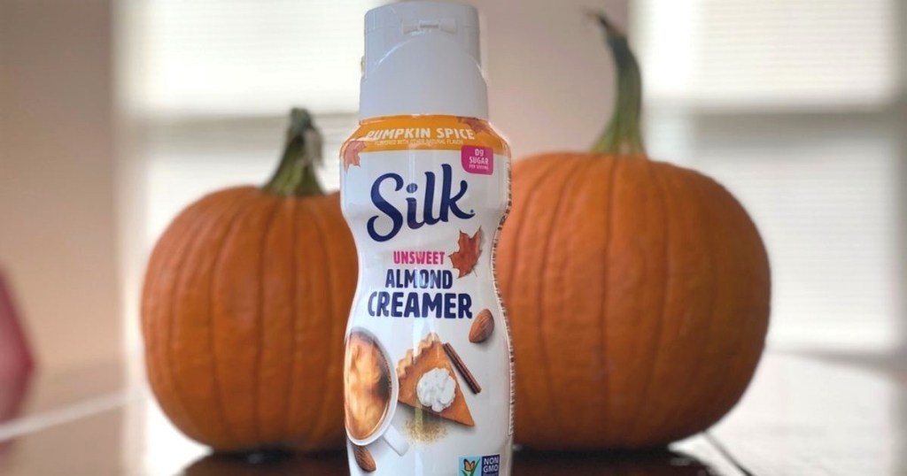 A pumpkin coffee creamer on a table next to some pumpkins