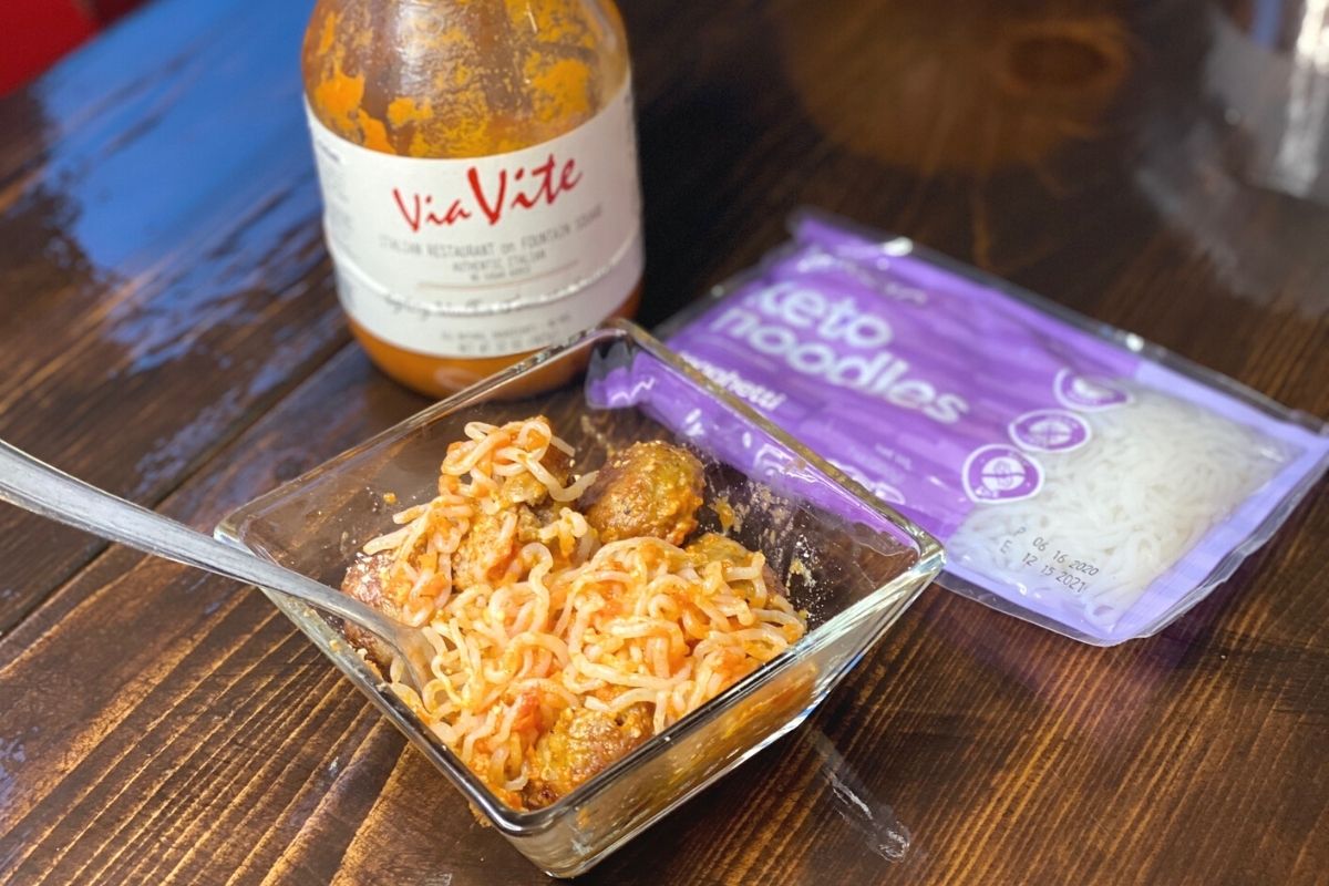 A bowl of spaghetti and meatballs next to a bag of noodles and sauce