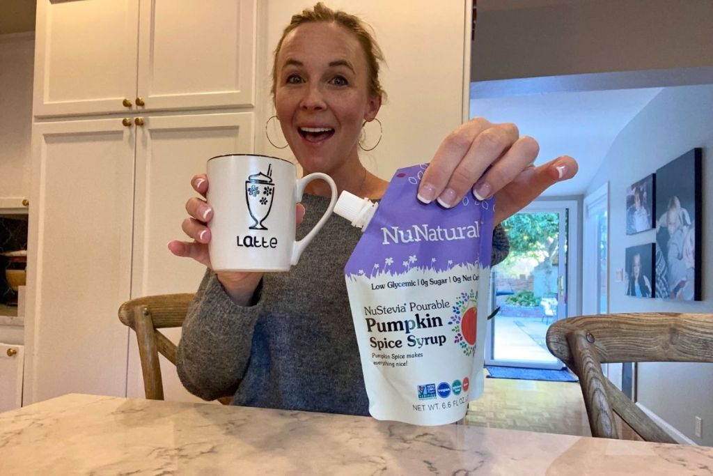 woman holding NuNaturals Pumpkin Spice syrup with coffee mug