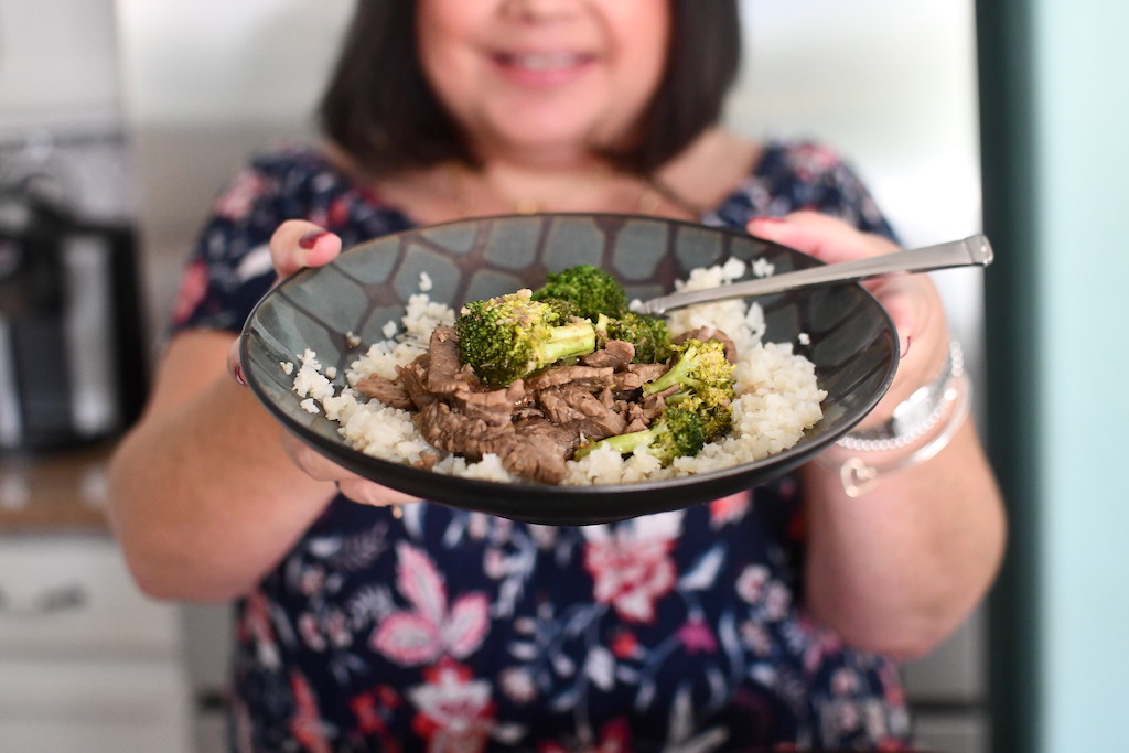 woman holding bowl of keto beef and broccoli 