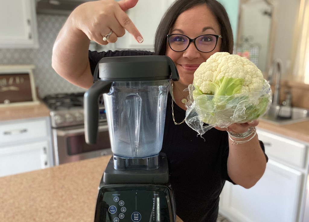  mujer sosteniendo cabeza de coliflor junto a la licuadora