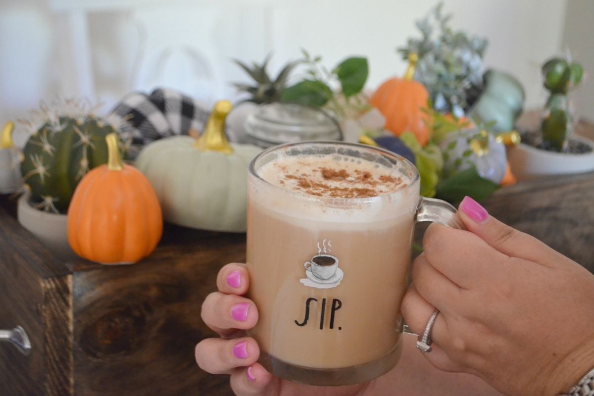 holding a glass coffee cup with NuNaturals Pumpkin Spice syrup in front of pumpkins