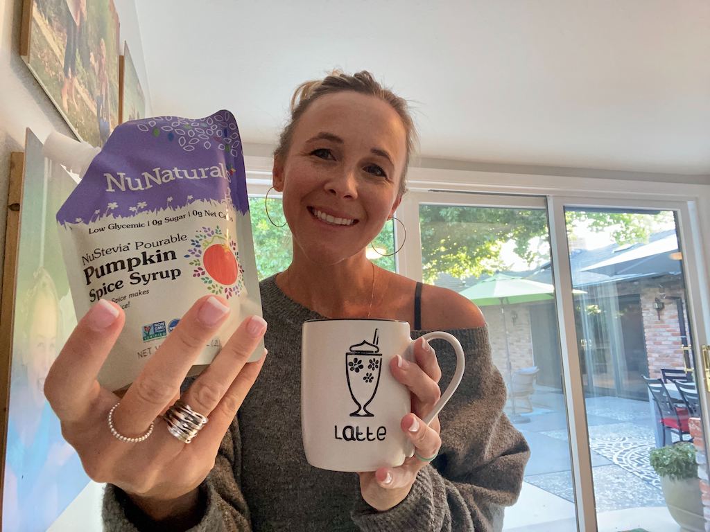 woman holding pumpkin spice syrup and latte mug 