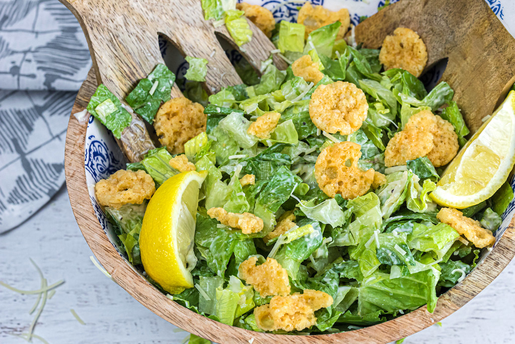tossing the finished salad with keto parmesan crisps in a bowl
