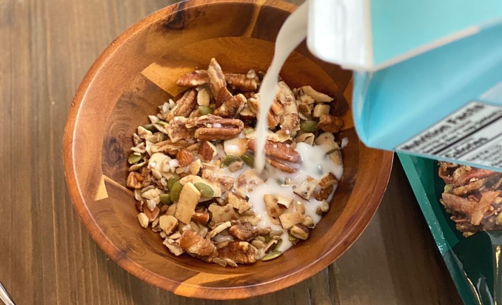 Pouring milk into a bowl of granola on a table