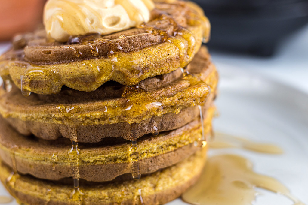 keto pumpkin chaffles stacked on plate with syrup and whipped cream