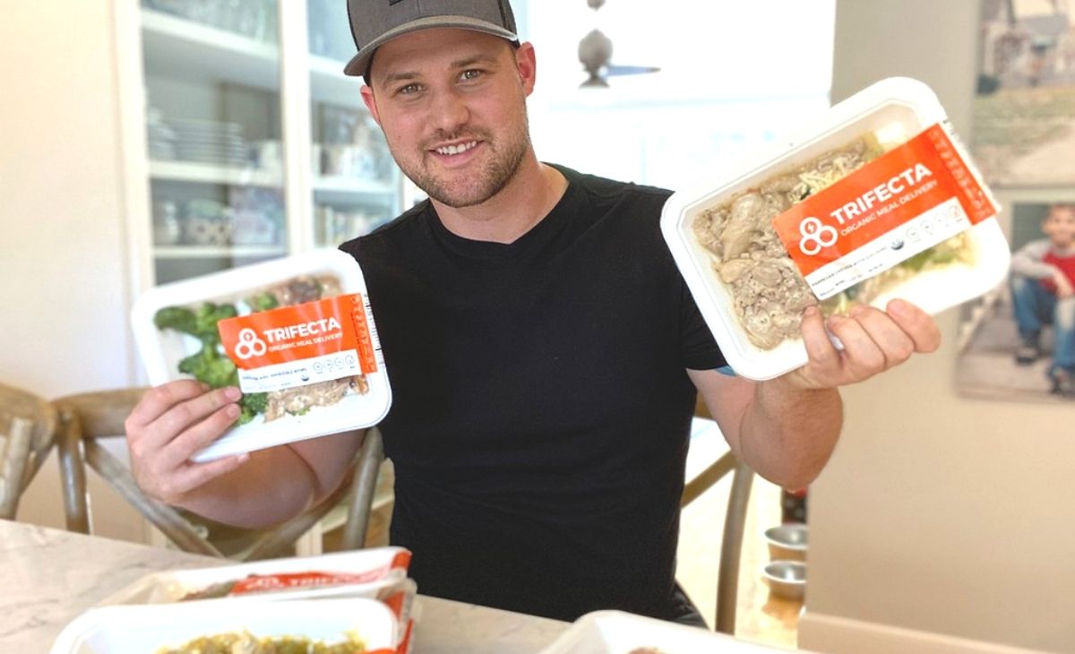 A man holding pre-made keto entrees in a kitchen