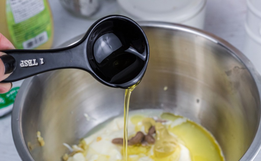 pouring olive oil into mixing bowl with other keto caesar dressing ingredients