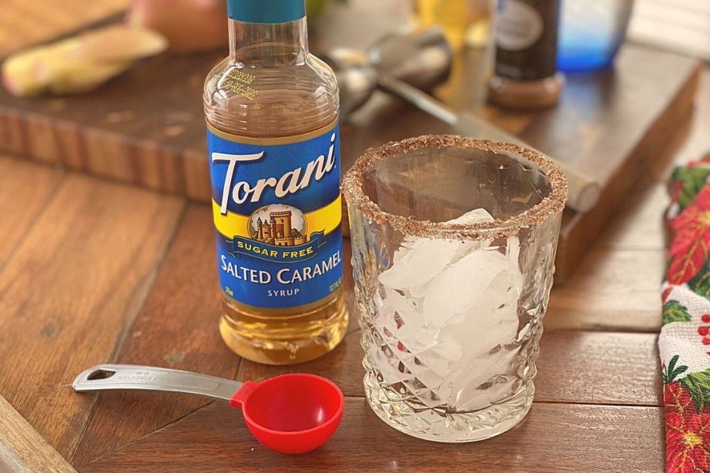 A glass of ice next to a measuring spoon and some flavored syrup