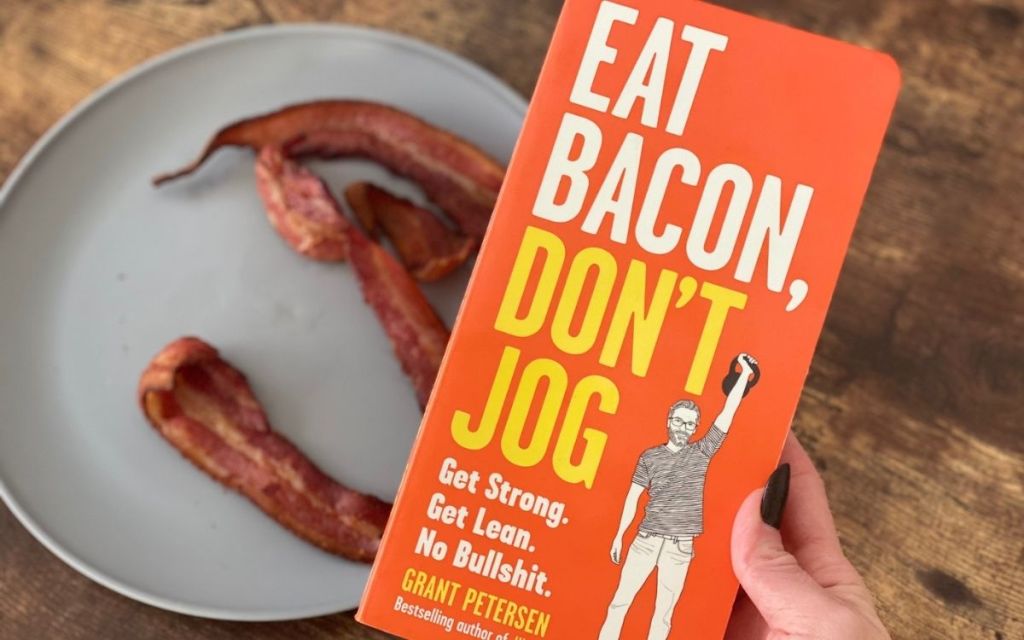 A hand holding a book over a plate of bacon on a table