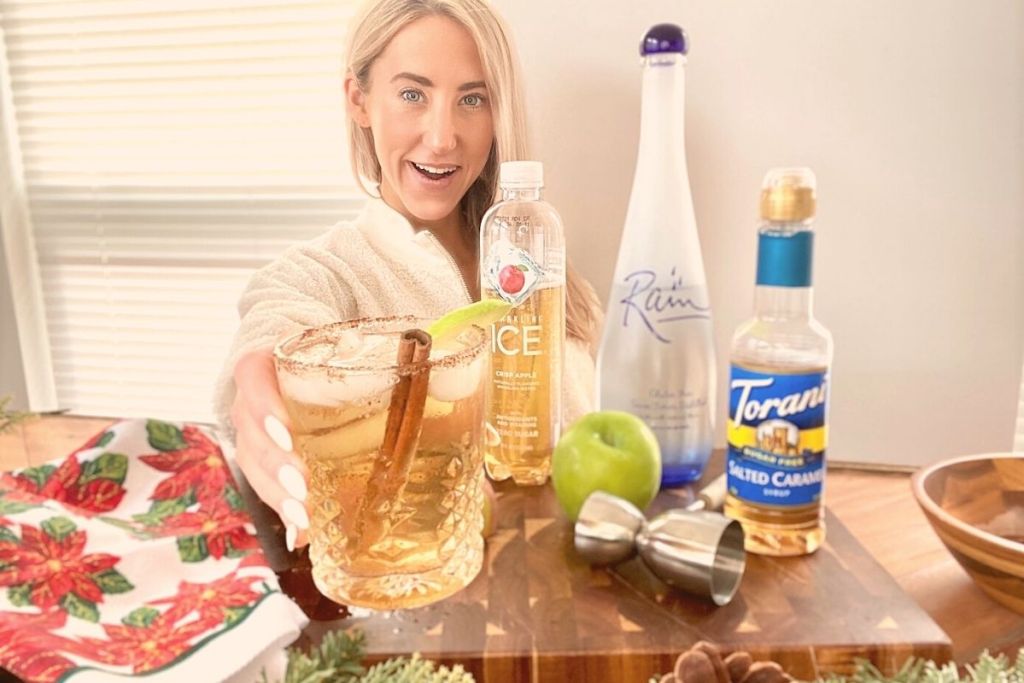 A woman holding a drink behind a bar next to drink ingredients