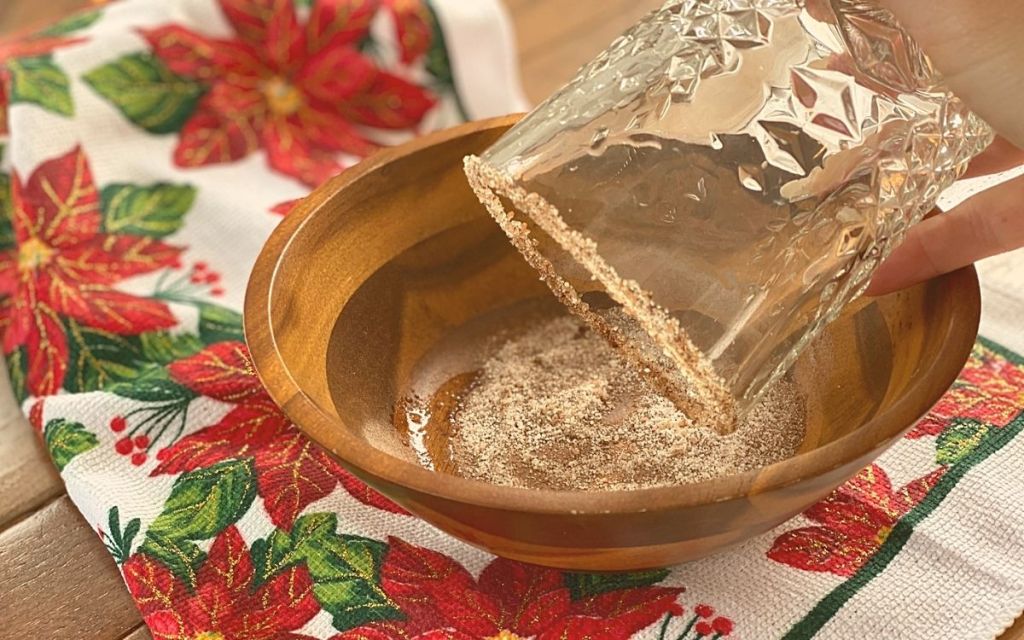 A hand dipping a glass into a bowl of cinnamon sugar for a cocktail rim