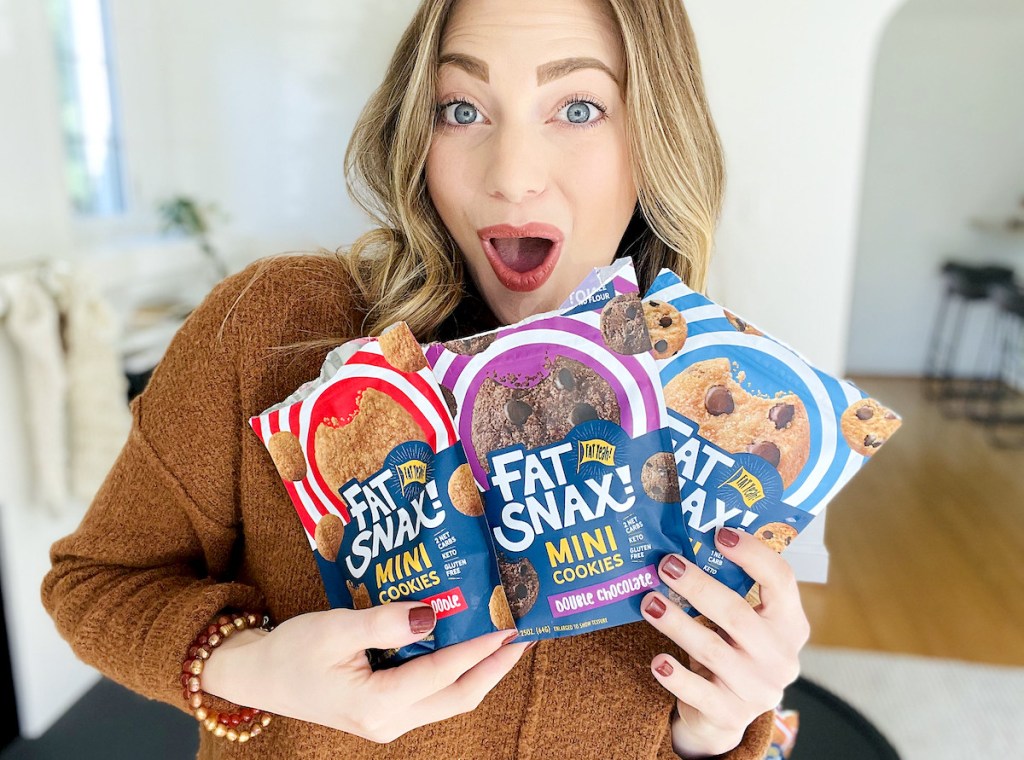 woman looking surprised holding three bags of keto fat snax cookies