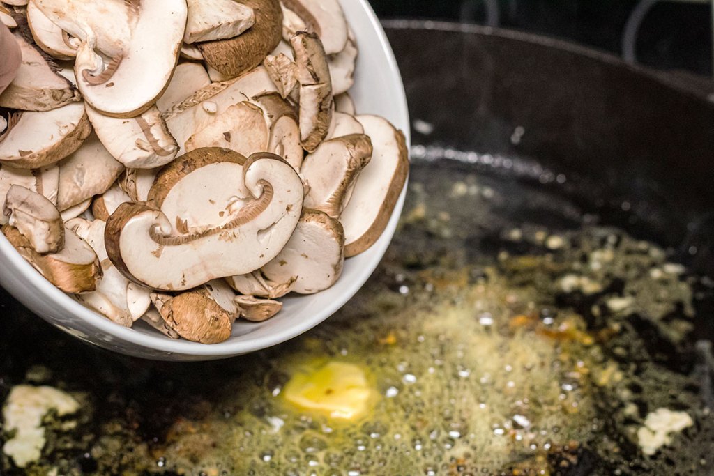 adding mushrooms to butter in cast iron pan