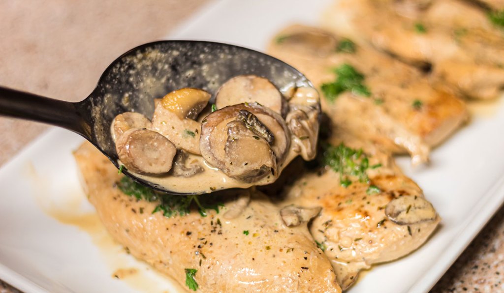 spooning mushrooms and sauce over keto chicken marsala