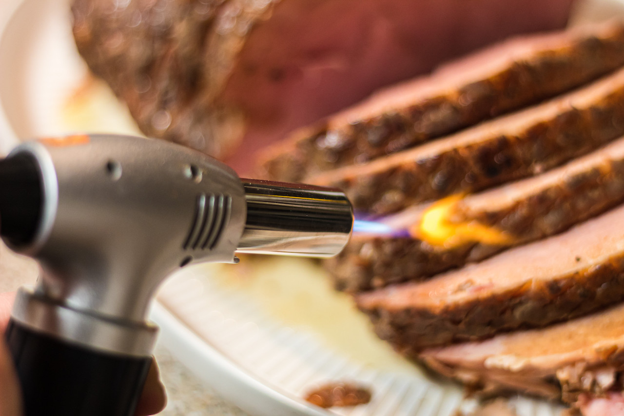 Using blow torch kitchen gadget to crisp ham edges 