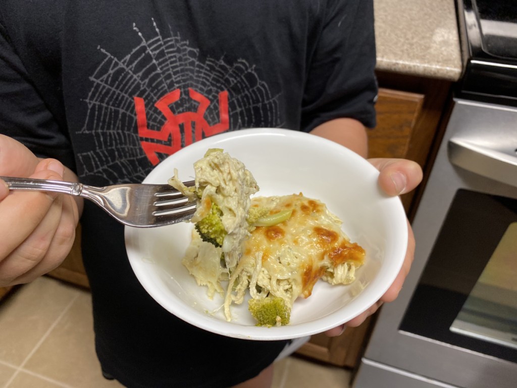 boy holding a bowl of keto chicken broccoli pesto casserole